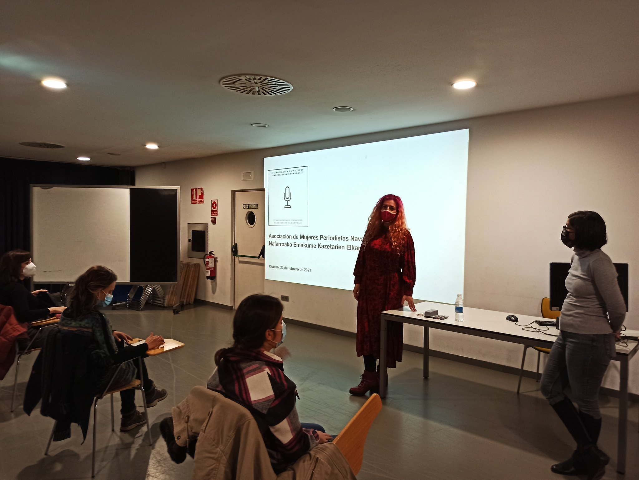 Presentación de la Asociación de Mujeres Periodistas. María Vallejo y Diana González presentan, ante una pantalla, los principios de la asociación en una sala con varias personas de espaldas a la cámara.