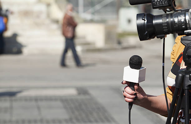 Aparece una cámara de televisión y una reportera con un micrófono de la mano.